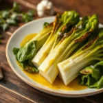 Roasted bok choy halves with charred edges, drizzled with sesame oil and garnished with sesame seeds, served on a white plate.